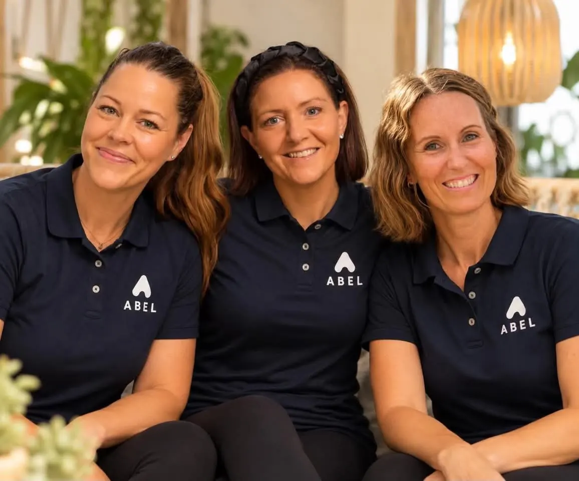 Tre instruktører fra ABEL i mørkeblå poloer med ABEL-logoen, i lys og grønn omgivelser